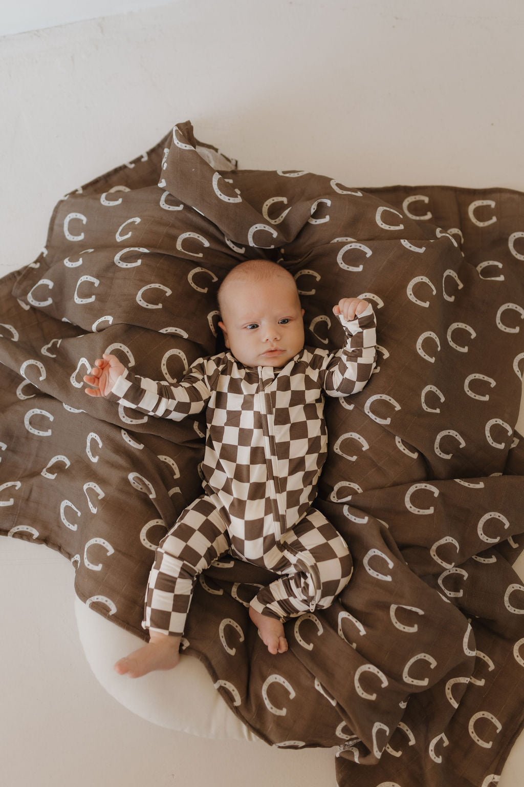 Baby in brown and white checkerboard bamboo zip pajamas from Dutton, lying on a cozy blanket.