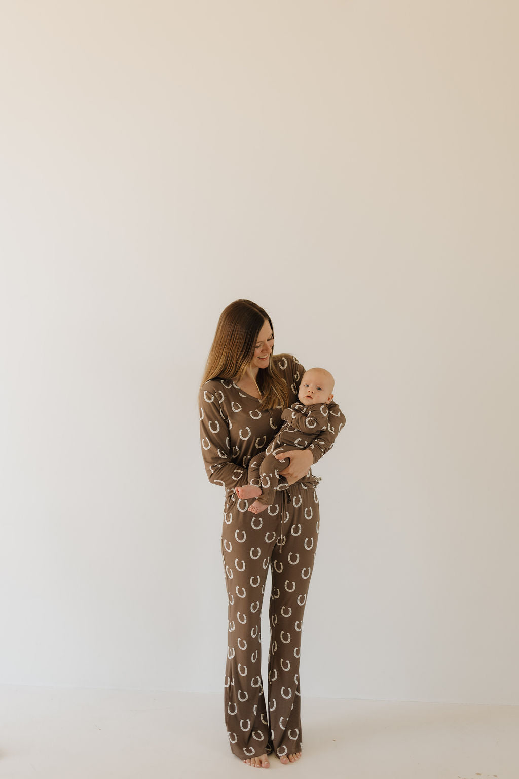Mom and baby wearing matching bamboo zip pajamas giddy up in a brown horseshoe print.