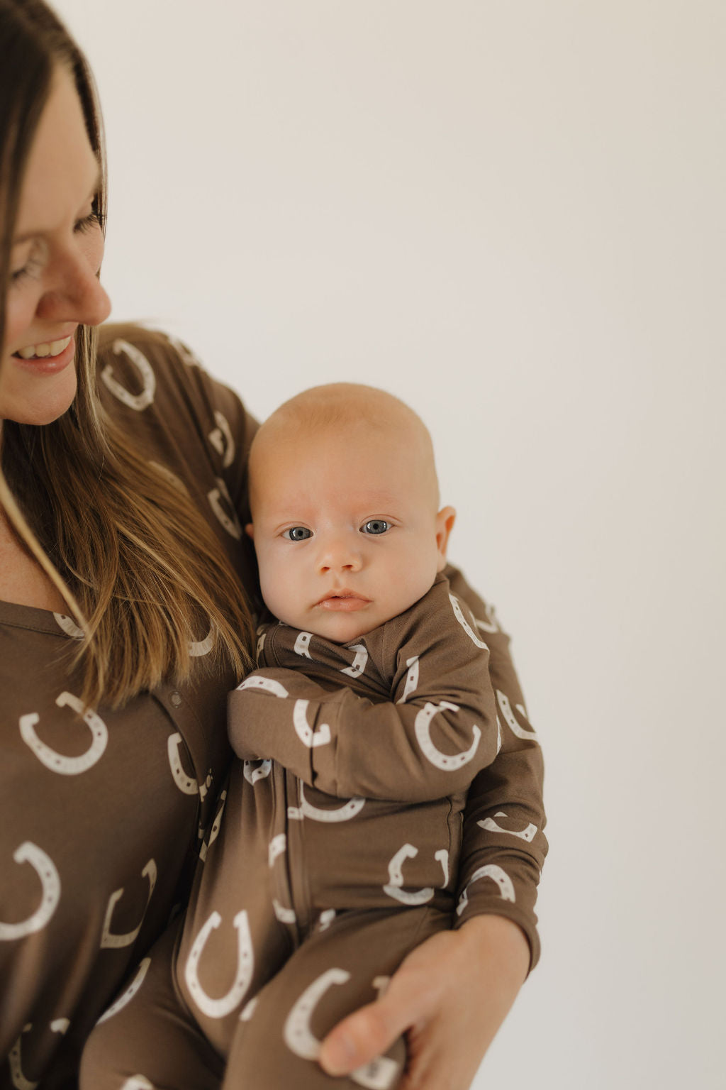 Baby in bamboo zip pajamas giddy up with horseshoe print, held by smiling parent, showcasing comfort and style.