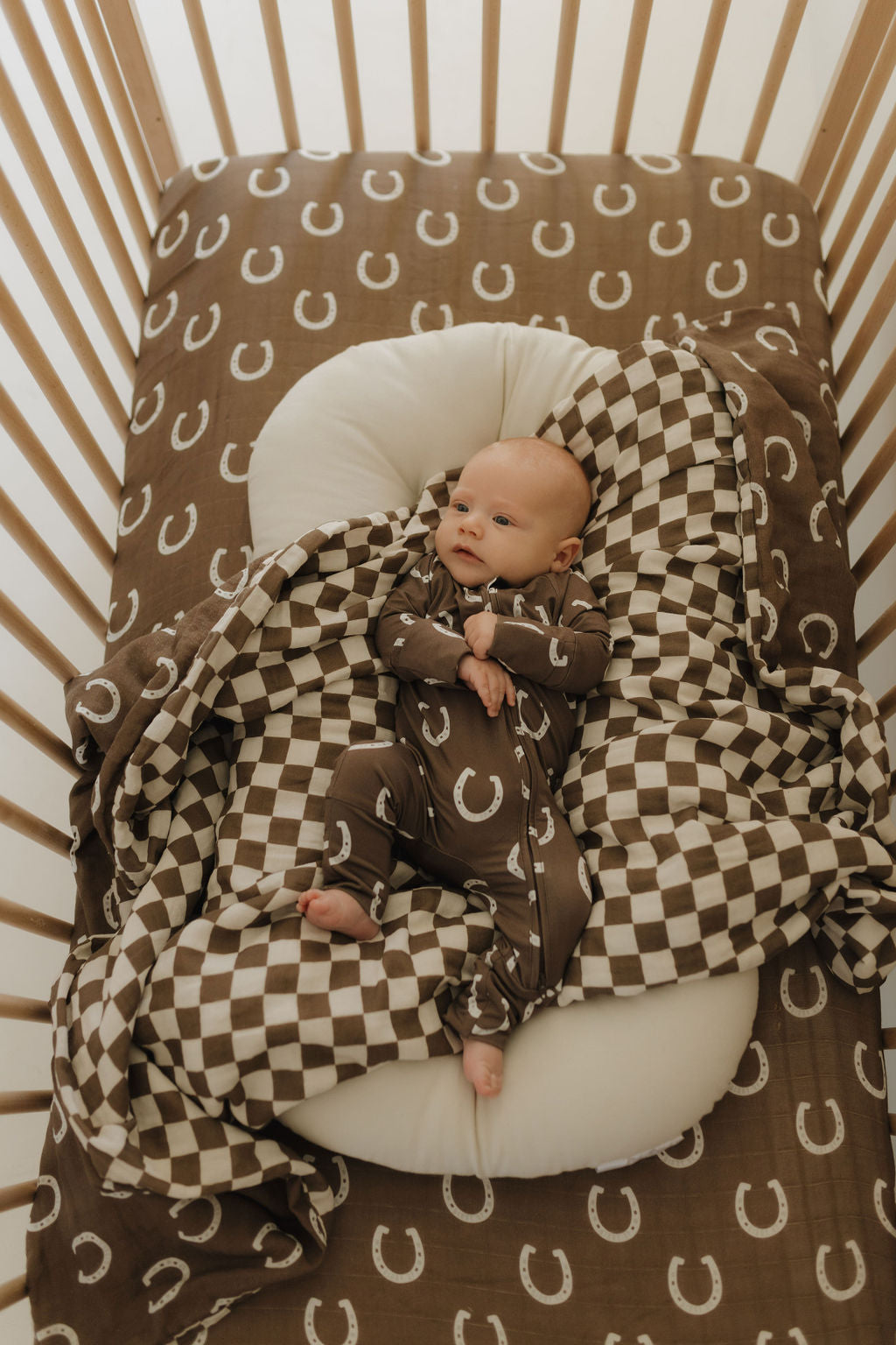 Baby wearing bamboo zip pajamas giddy up in crib with horseshoe printed blanket.