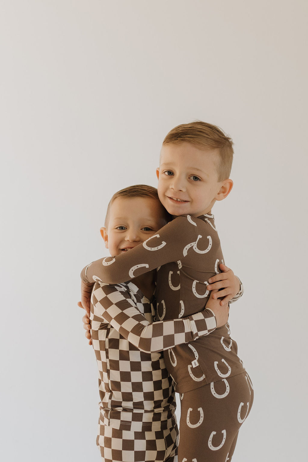 Kids in bamboo two-piece pajamas giddy up, hugging, showcasing playful patterns and cozy comfort.