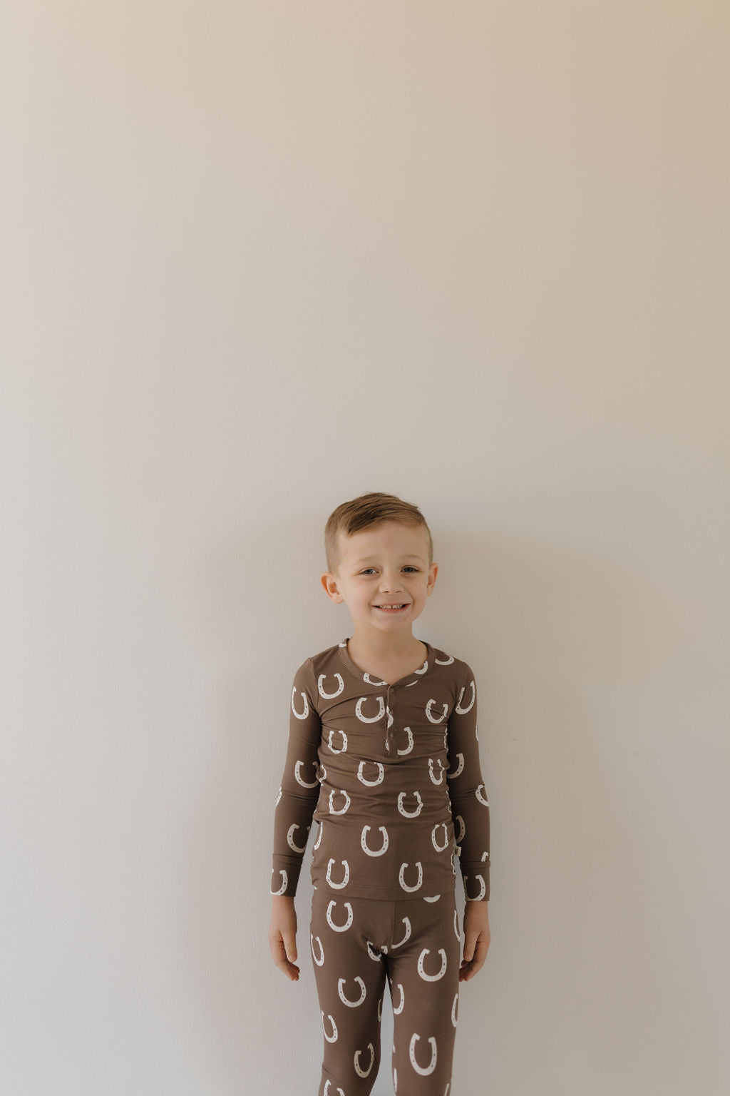 Smiling child wearing bamboo two-piece pajamas giddy up with horseshoe print under natural light.