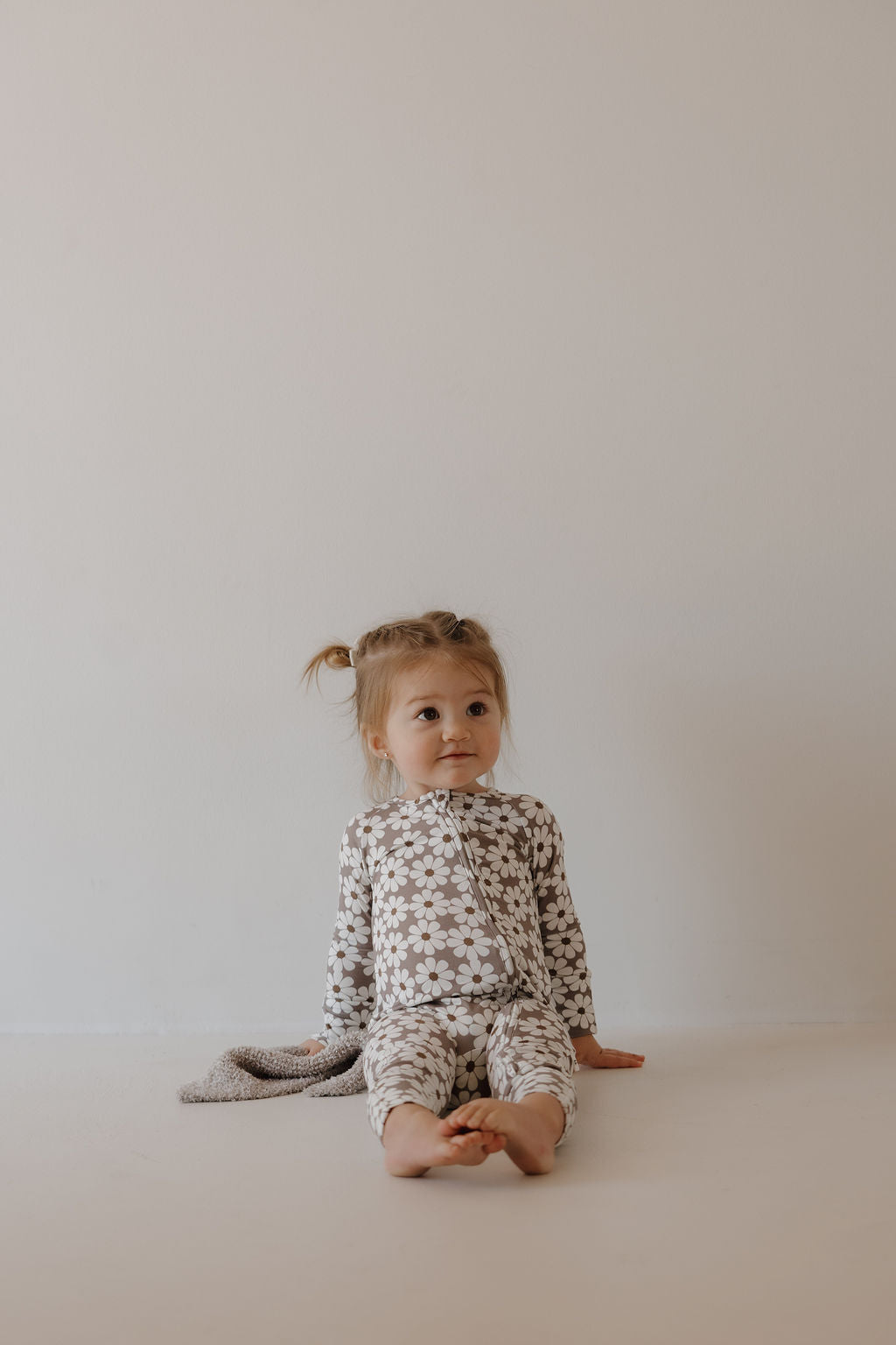 Baby wearing bamboo zip pajamas darlin' with a playful brown and white floral print, sitting on a neutral background.