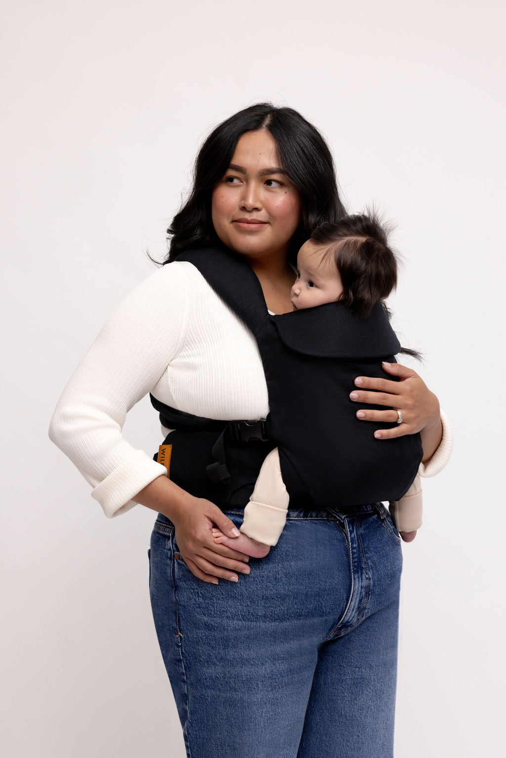 A woman wearing the Raven Aerial Carrier, confidently holding her baby, showcasing its sleek black design and comfort.