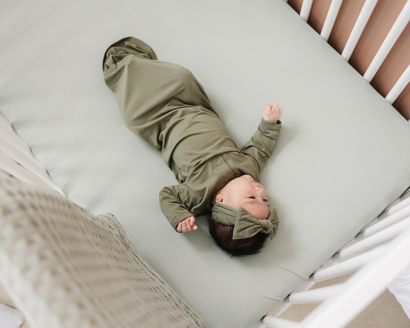 Baby lying peacefully on a sage bamboo crib sheet in a stylish nursery.