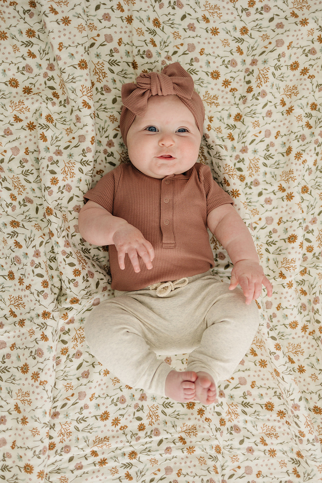 Baby wearing a dusty rose organic cotton ribbed bodysuit and headband, surrounded by floral patterned blanket.