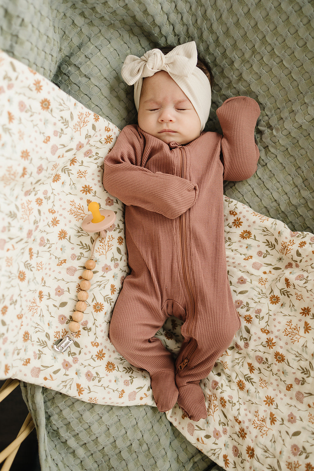 Baby peacefully sleeping in dusty rose organic cotton ribbed zipper sleeper on a floral blanket.