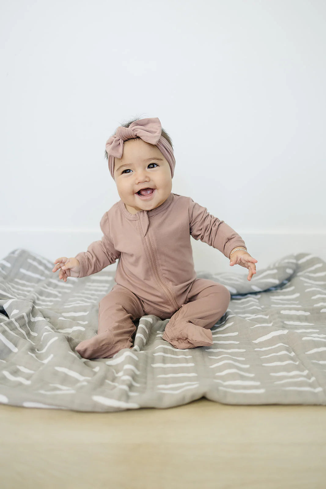 Bamboo baby pajamas dusty rose footed zipper on a smiling baby sitting on a blanket.