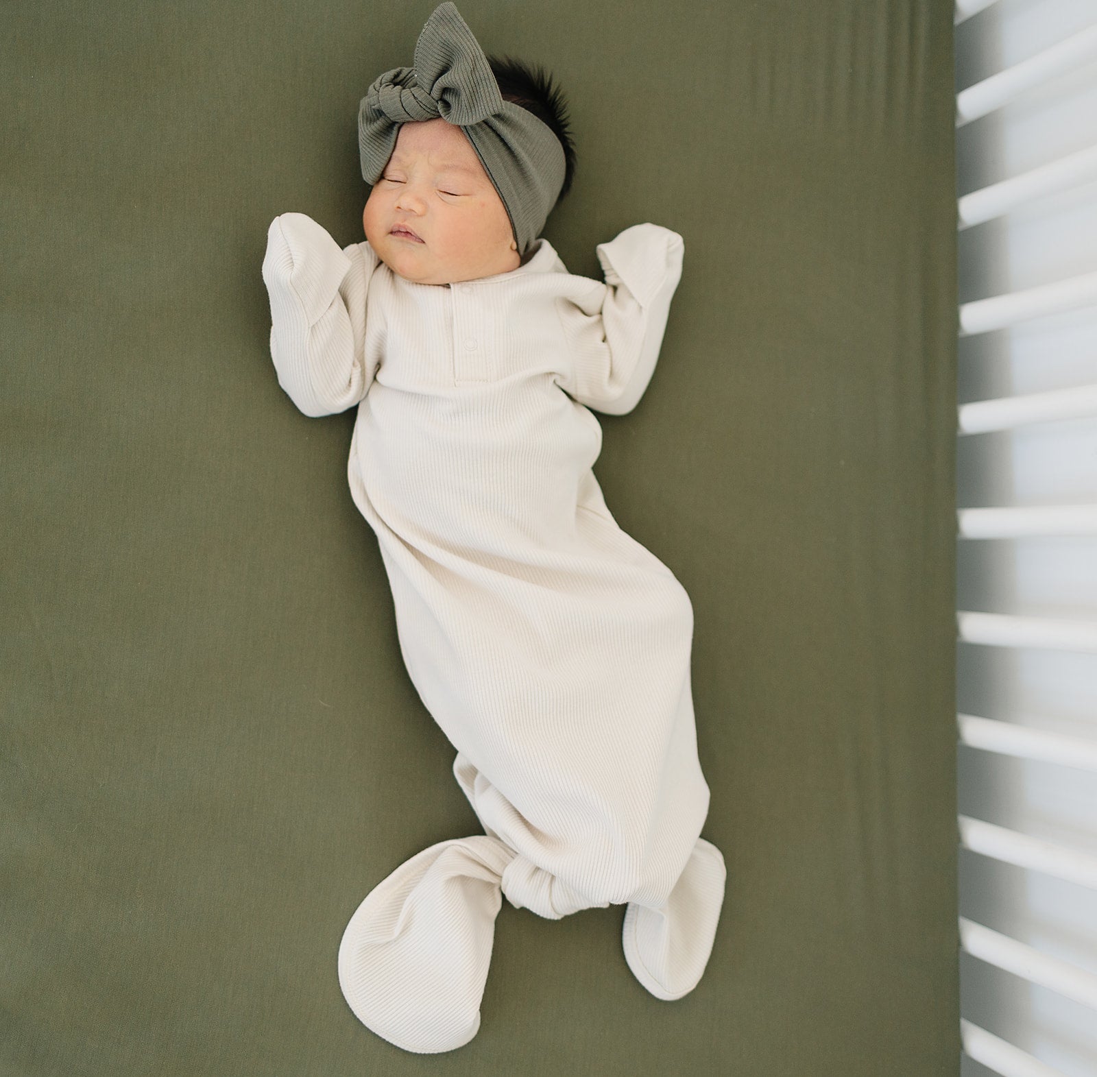 Newborn in a vanilla organic baby knot gown with a cute headband, perfect for cozy and stylish infant snuggles.