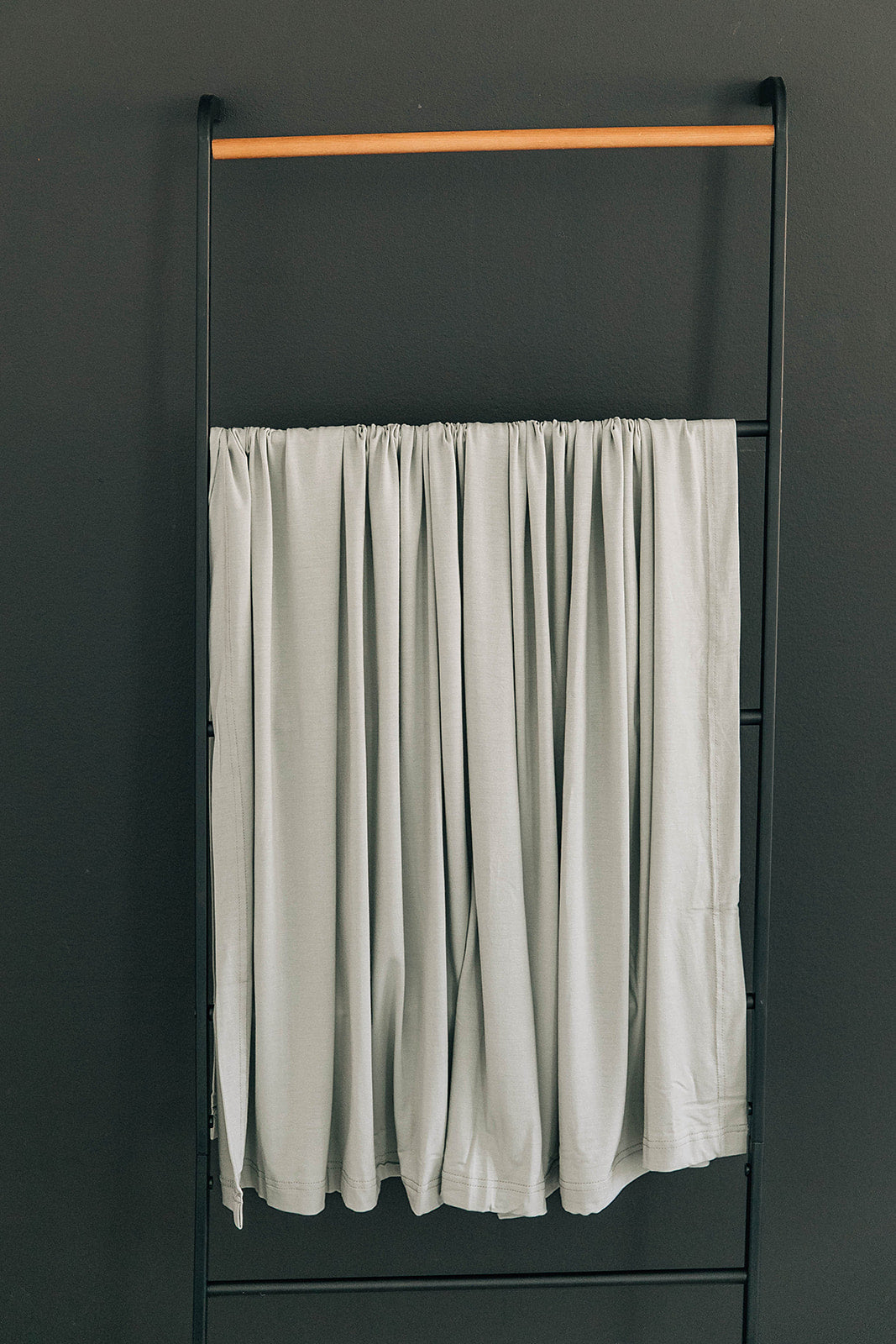 Bamboo Stretch Swaddle Sage hanging on a metal rack, showcasing its soft, breathable fabric in a tranquil sage color.