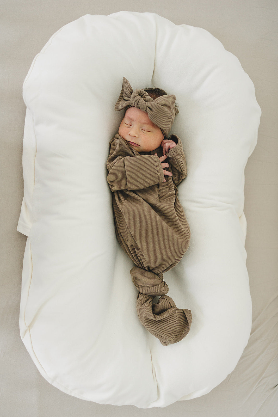 Organic baby knot gown in cocoa, featuring a newborn sleeping peacefully with a matching bow, perfect for cozy comfort.