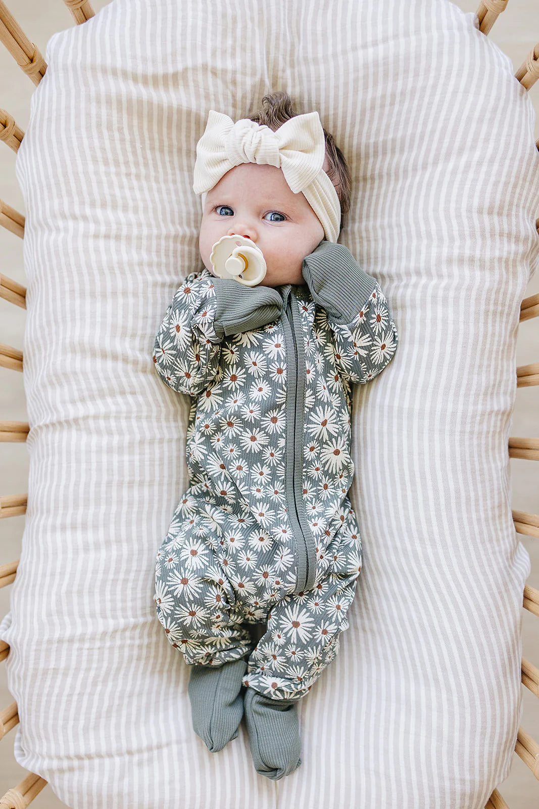 Baby in dark green ribbed bamboo zipper onesie with daisy print, wearing a bow headband.