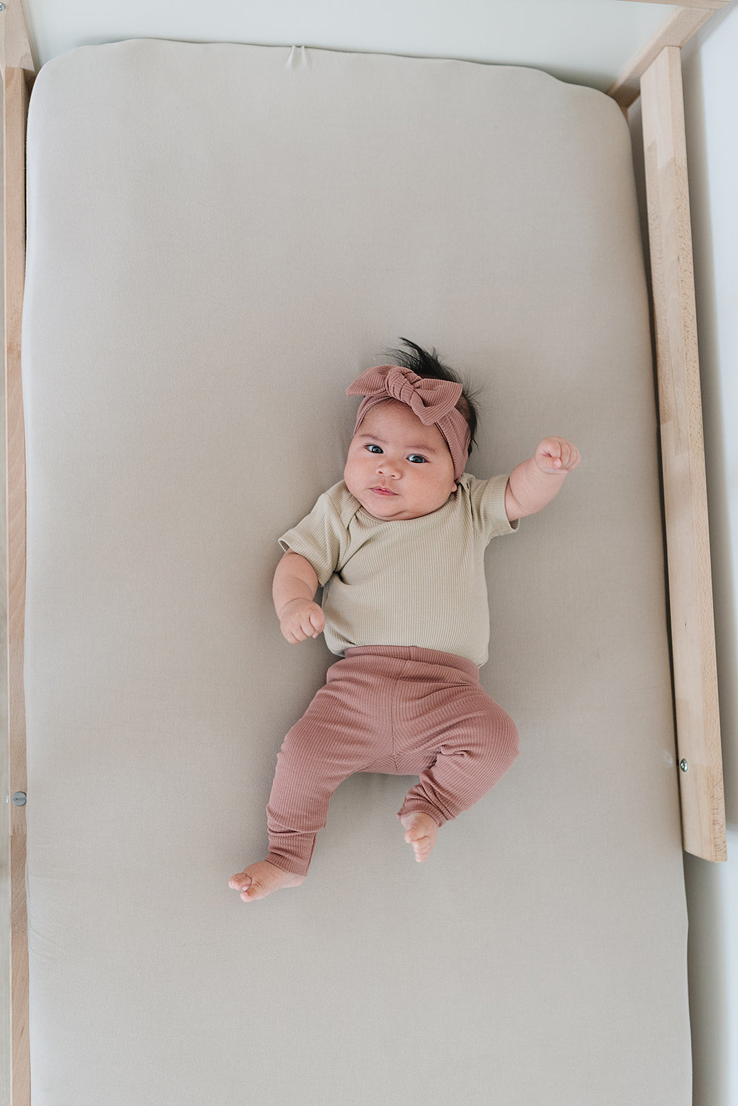 Baby in dusty rose organic leggings and matching headband on a crib, showcasing organic baby leggings style and comfort.