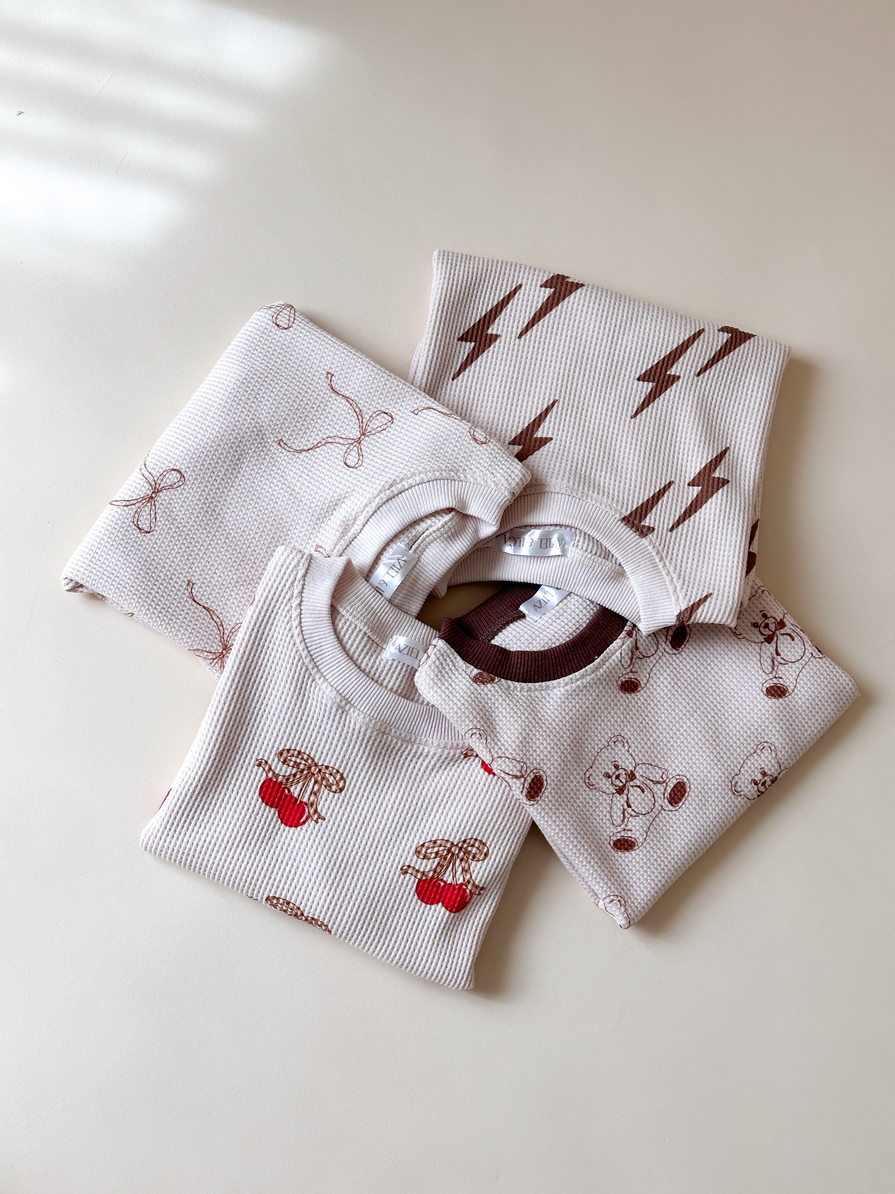 Adorable Bolt, Bow, Cherry and Bear Print Baby Waffle Sets stacked together, perfect for summer outfits.