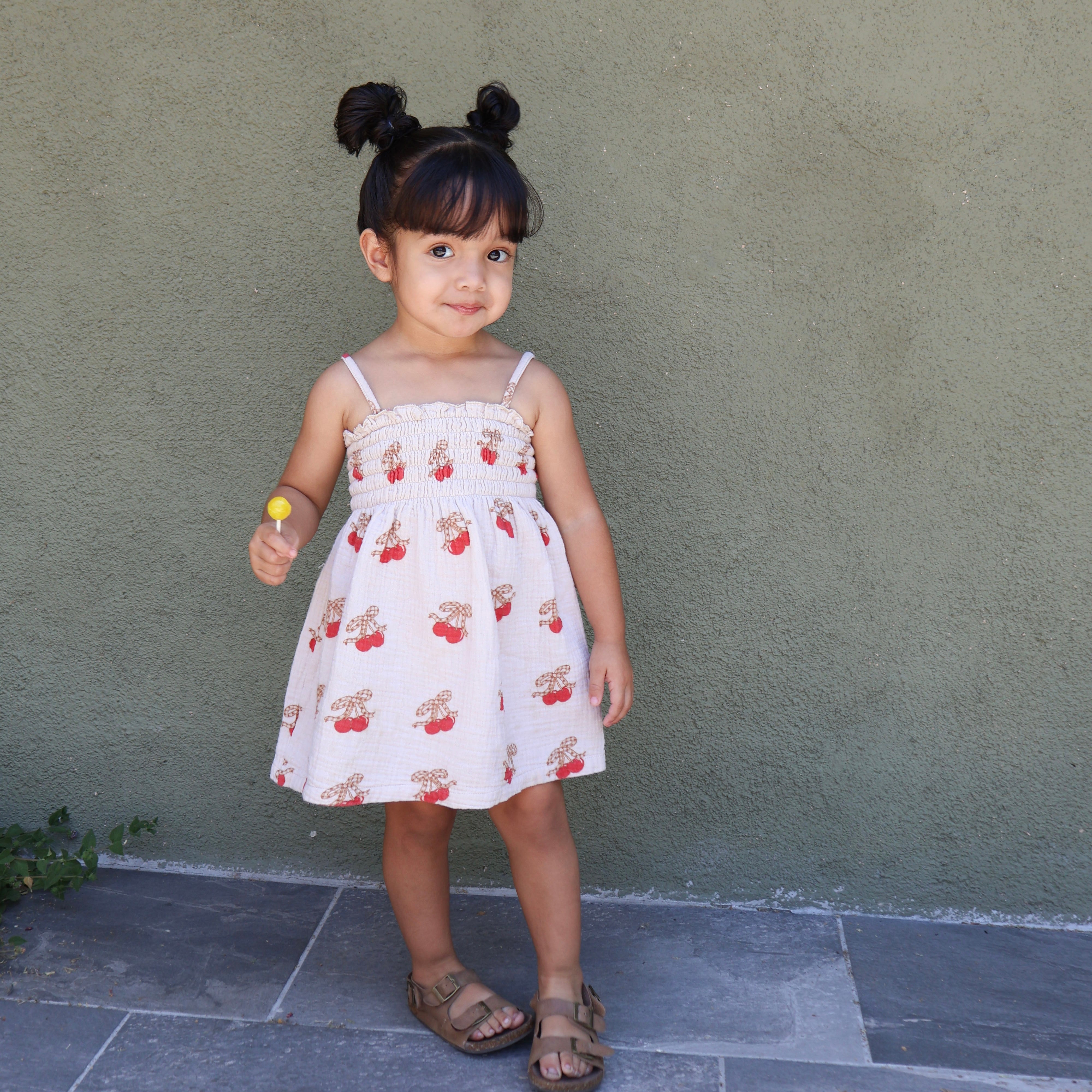 Child wearing a Printed Smocked Dress with cherry print, twirling joyfully in a playful outdoor setting.