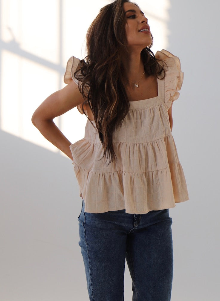 Model wearing a light beige ruffled sleeveless top paired with blue jeans, captured in a bright atmosphere.