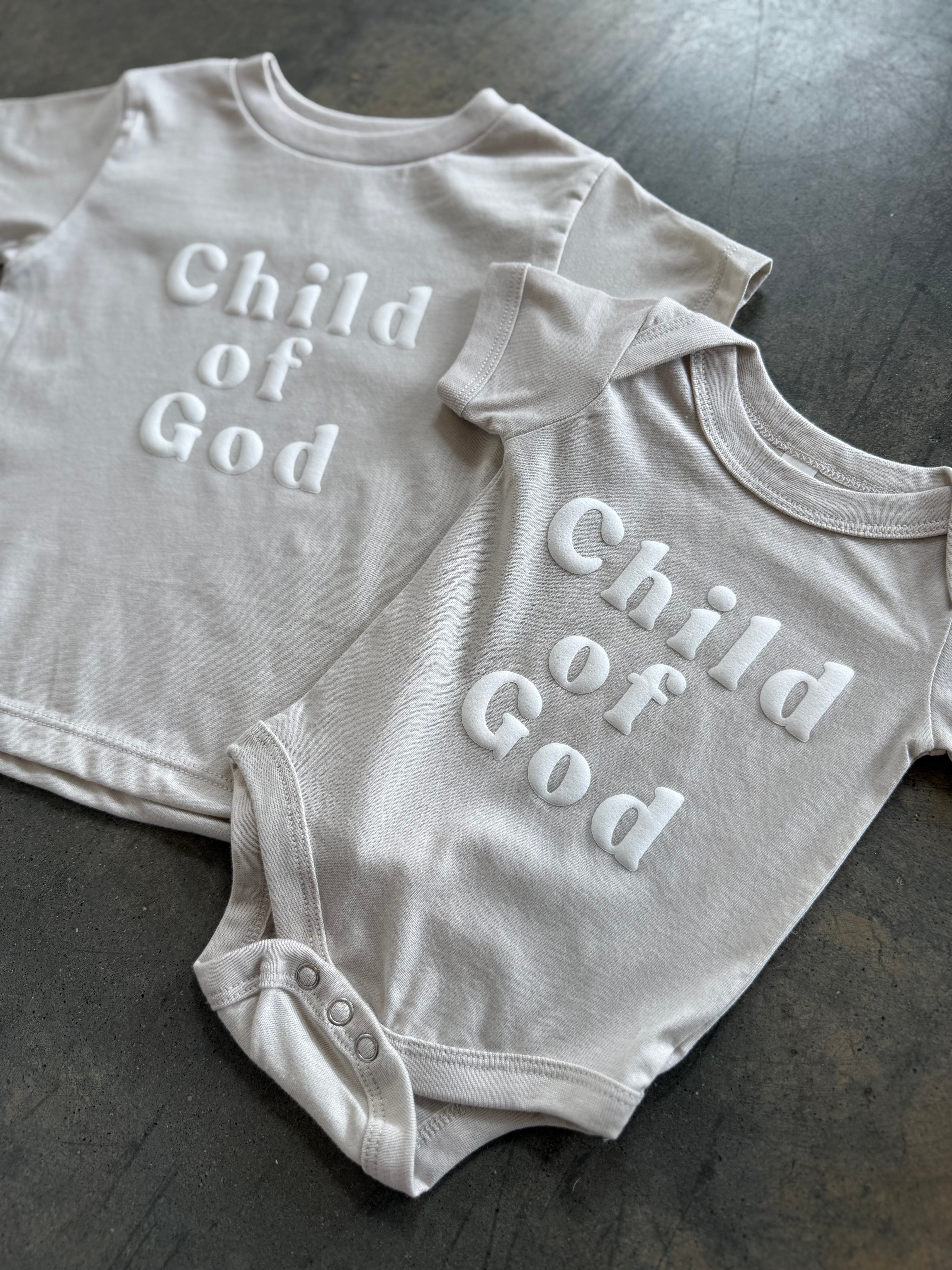 Child of God Onesie laying on dark surface 