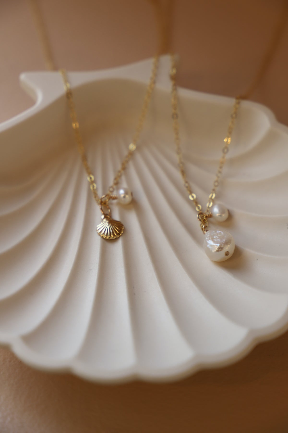 Double pearl drop necklace on a shell dish, featuring gold-toned chain and delicate freshwater pearls.