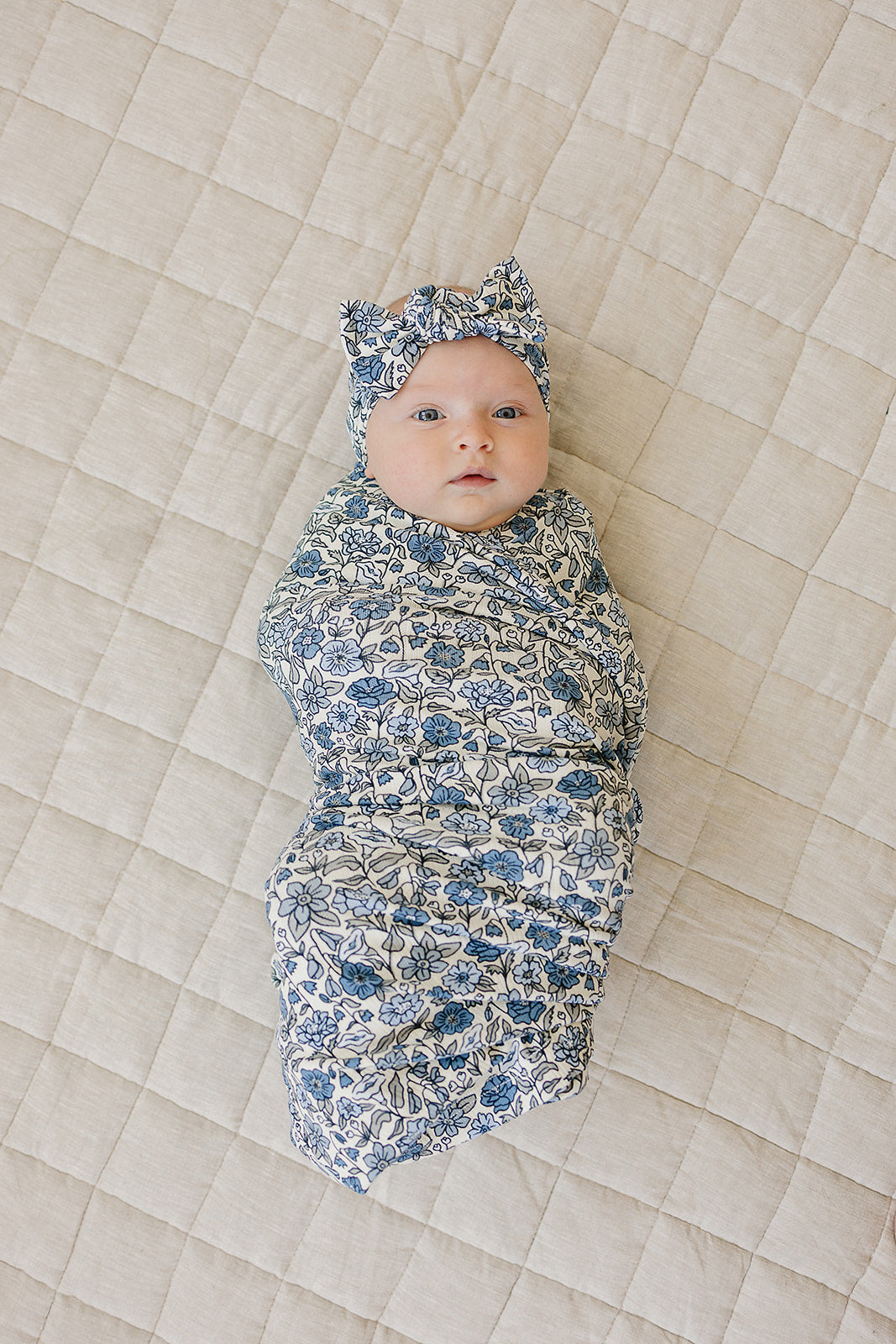 Bamboo Stretch Swaddle Bluebell Pointelle on a baby, featuring a floral pattern and matching headband.