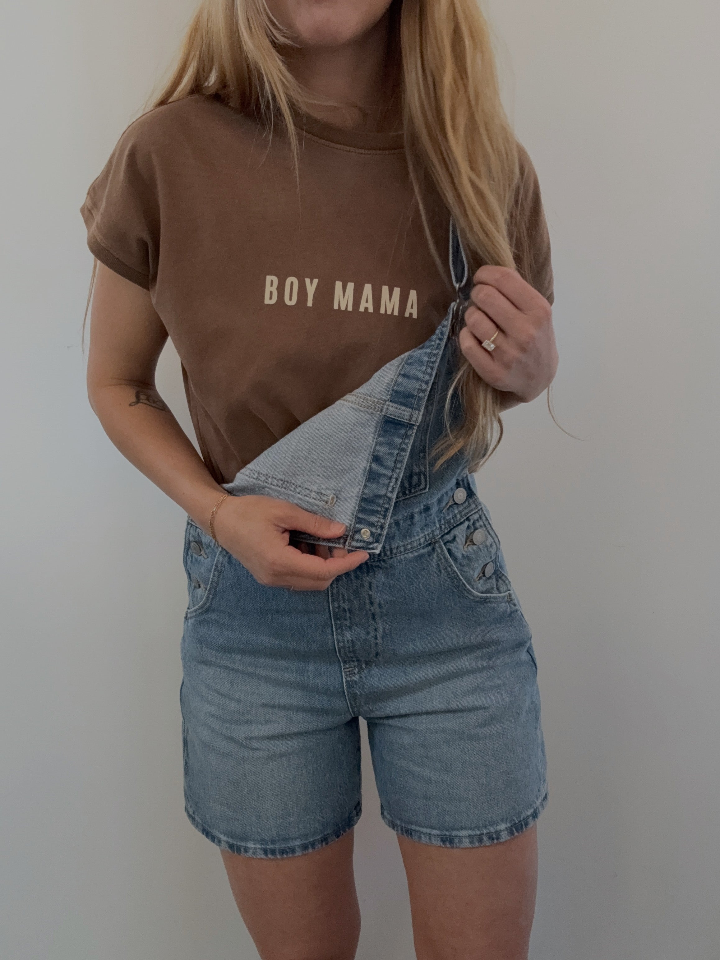 Model wearing a brown 'Boy Mama' tee with denim overalls, showcasing trendy mom style and casual comfort.