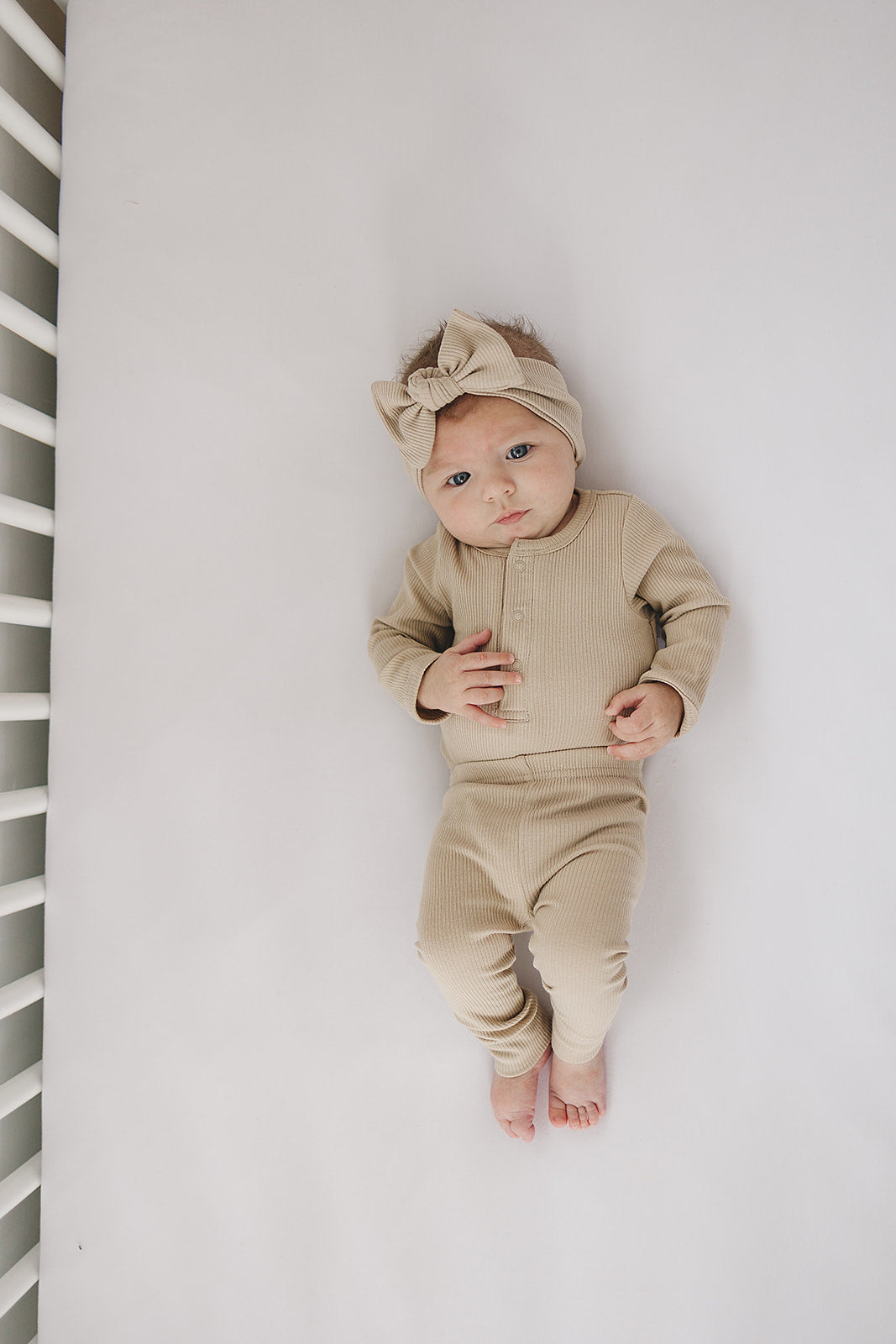 Baby wearing oatmeal organic leggings and matching headband, lying on a white surface.
