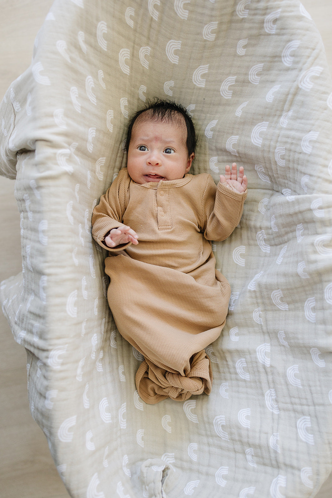 Newborn in cozy cafe organic cotton ribbed knot gown, lying in a soft blanket with rainbow patterns.