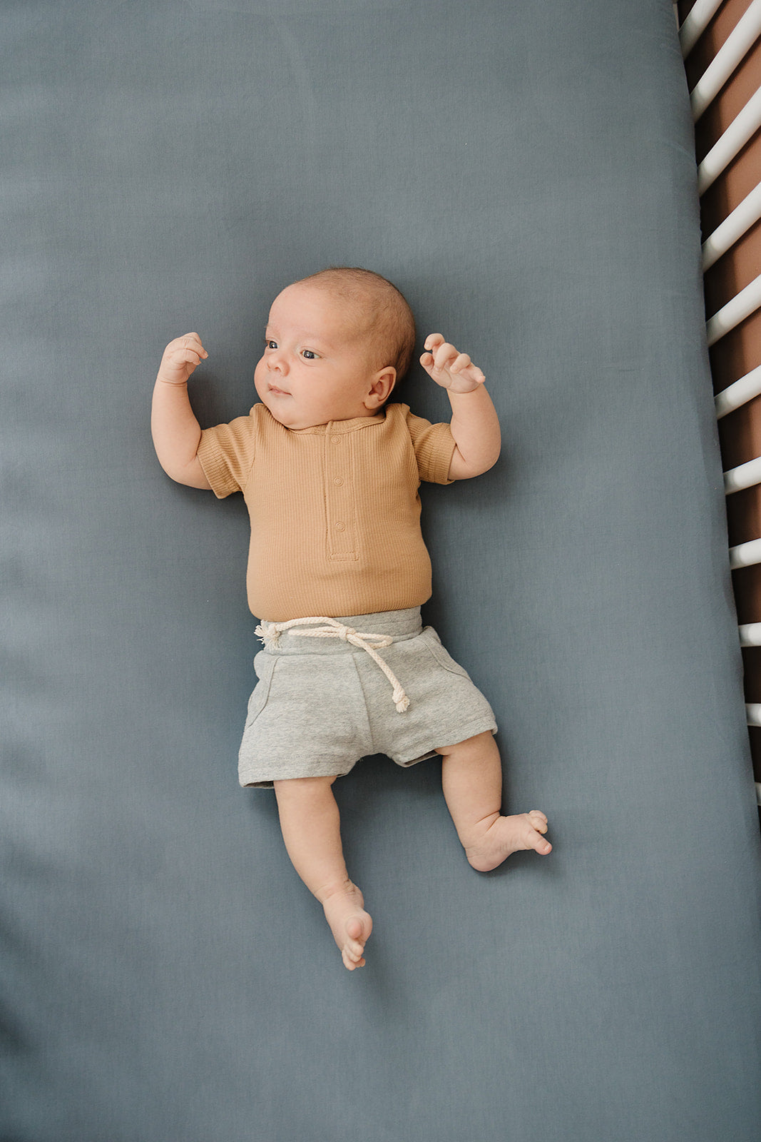 Organic baby bodysuit in cozy cafe shade on a baby laying on a soft gray surface.