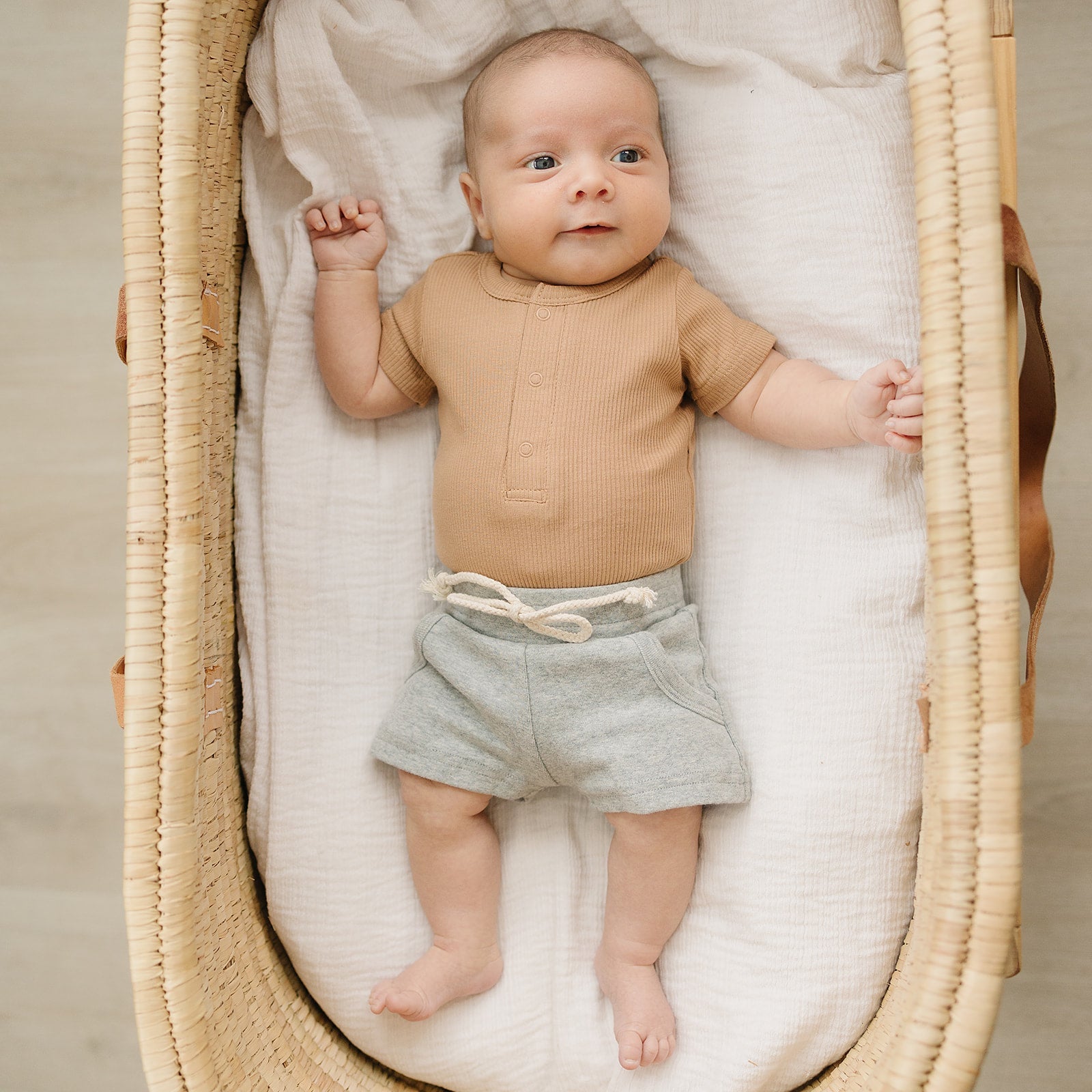 Organic baby bodysuit in cozy cafe shade, worn by an infant in a basket, showcasing comfort and style.