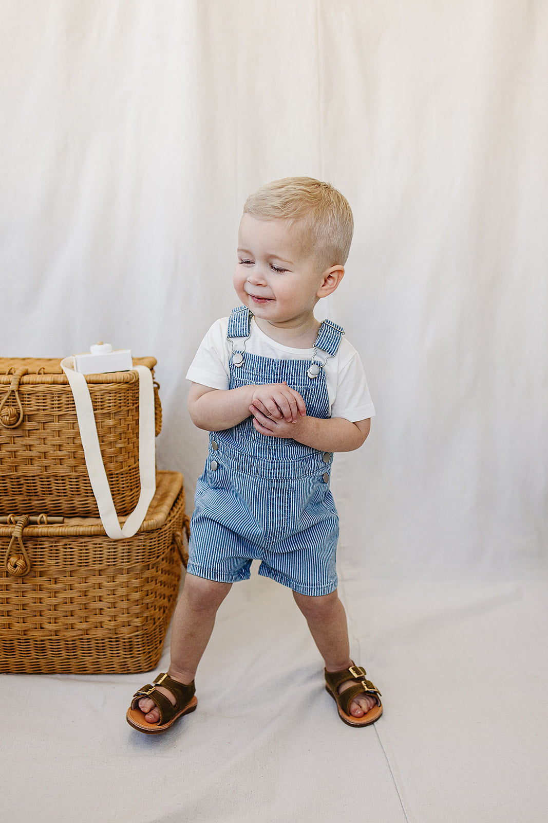 Smiling toddler in blue stripe short overalls, perfect for summer playdates and beach days.
