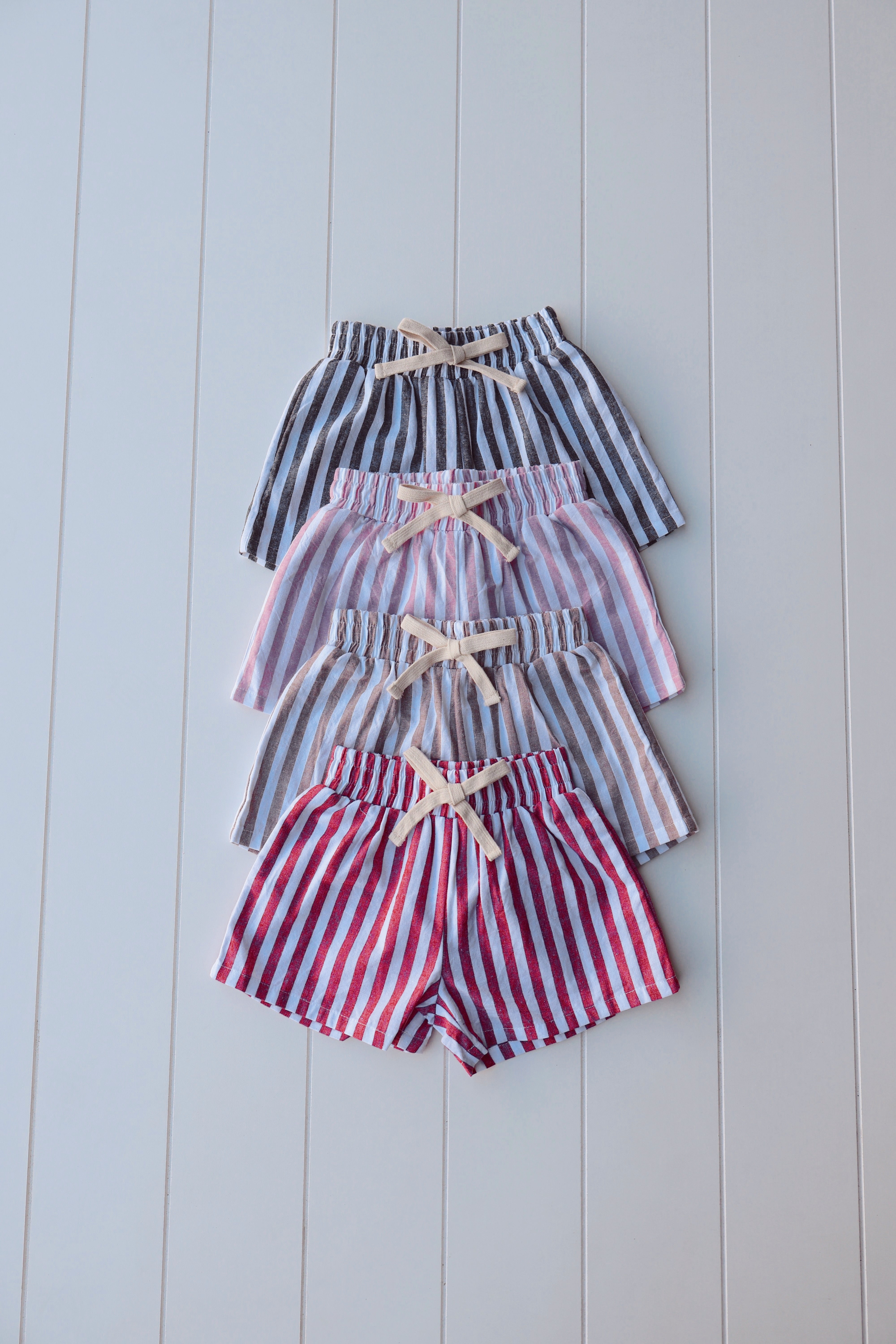 Set of three pairs of striped shorts in red, white, and blue on a light wooden background.