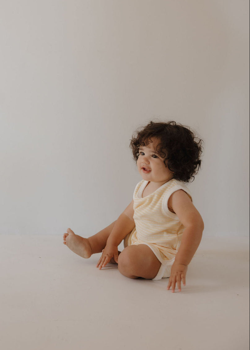 Toddler wearing a soft creamsicle two-piece terry cloth summer tank and short set sitting on the floor.