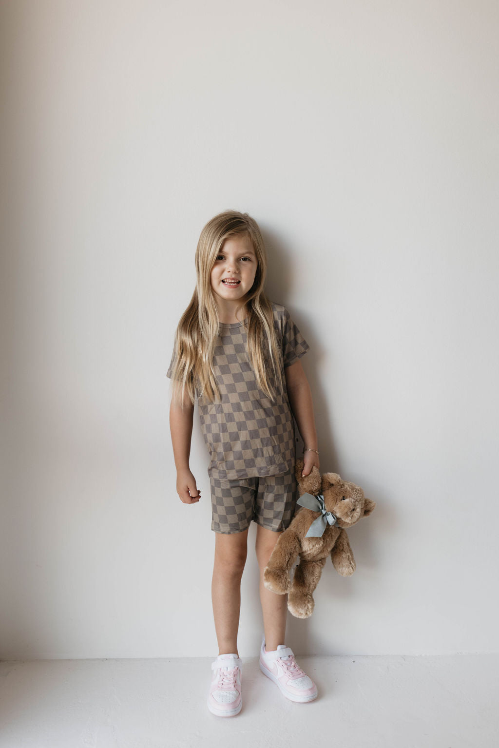 Toddler wearing bamboo short set in faded brown checkerboard with teddy bear, showcasing comfy summer style.