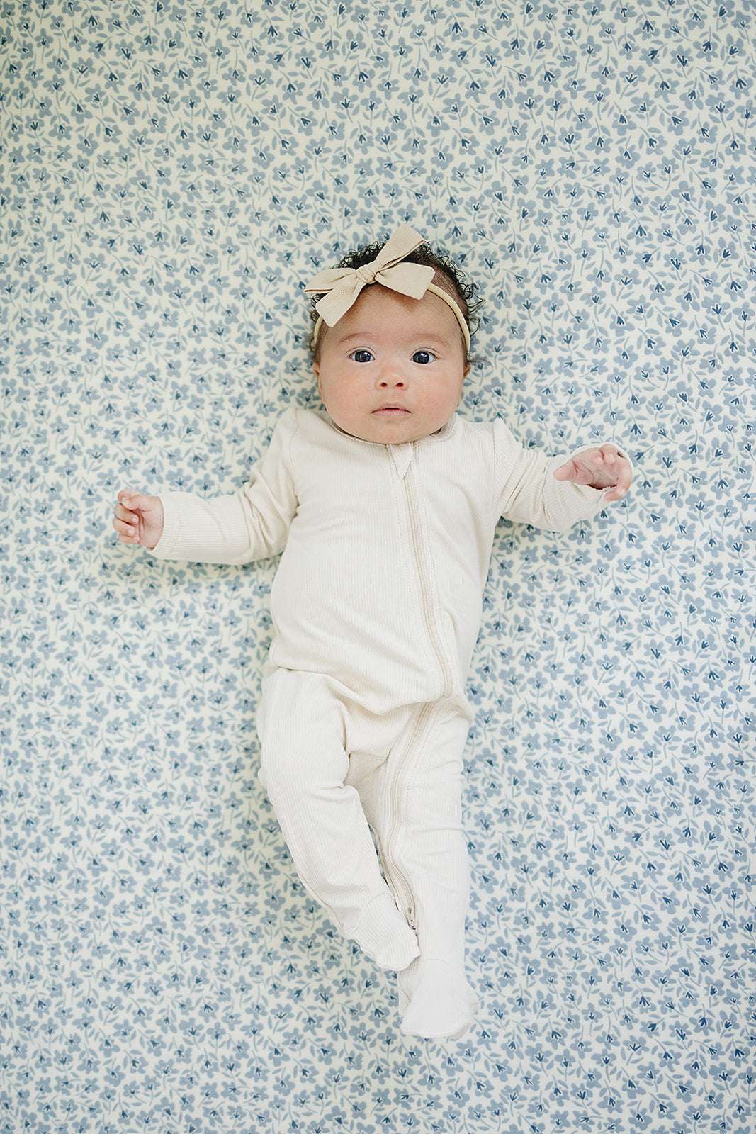 Baby lying on blue blossom muslin crib sheet, showcasing the soft design and comfort of the Muslin Crib Sheet.