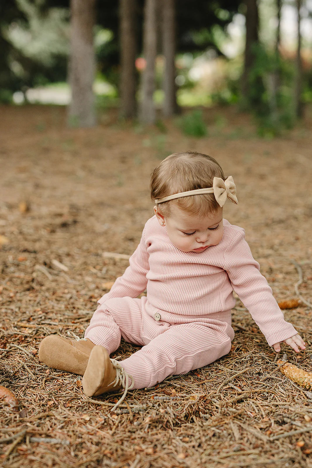 Adorable baby wearing a waffle knit baby bodysuit set, pink, sitting on the ground in a natural setting.