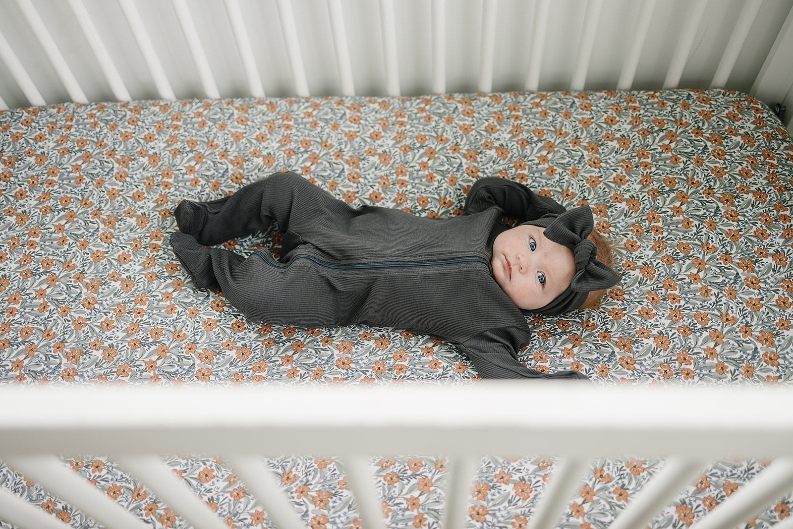 Baby lying on Dainty Meadow Floral bamboo crib sheet in a crib.