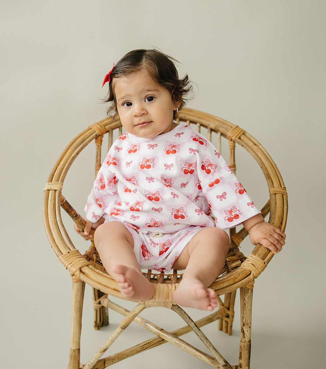 Baby wearing a Checkered Cherry shorts set, sitting on a rattan chair, showcasing playful cherry print and summer vibes.