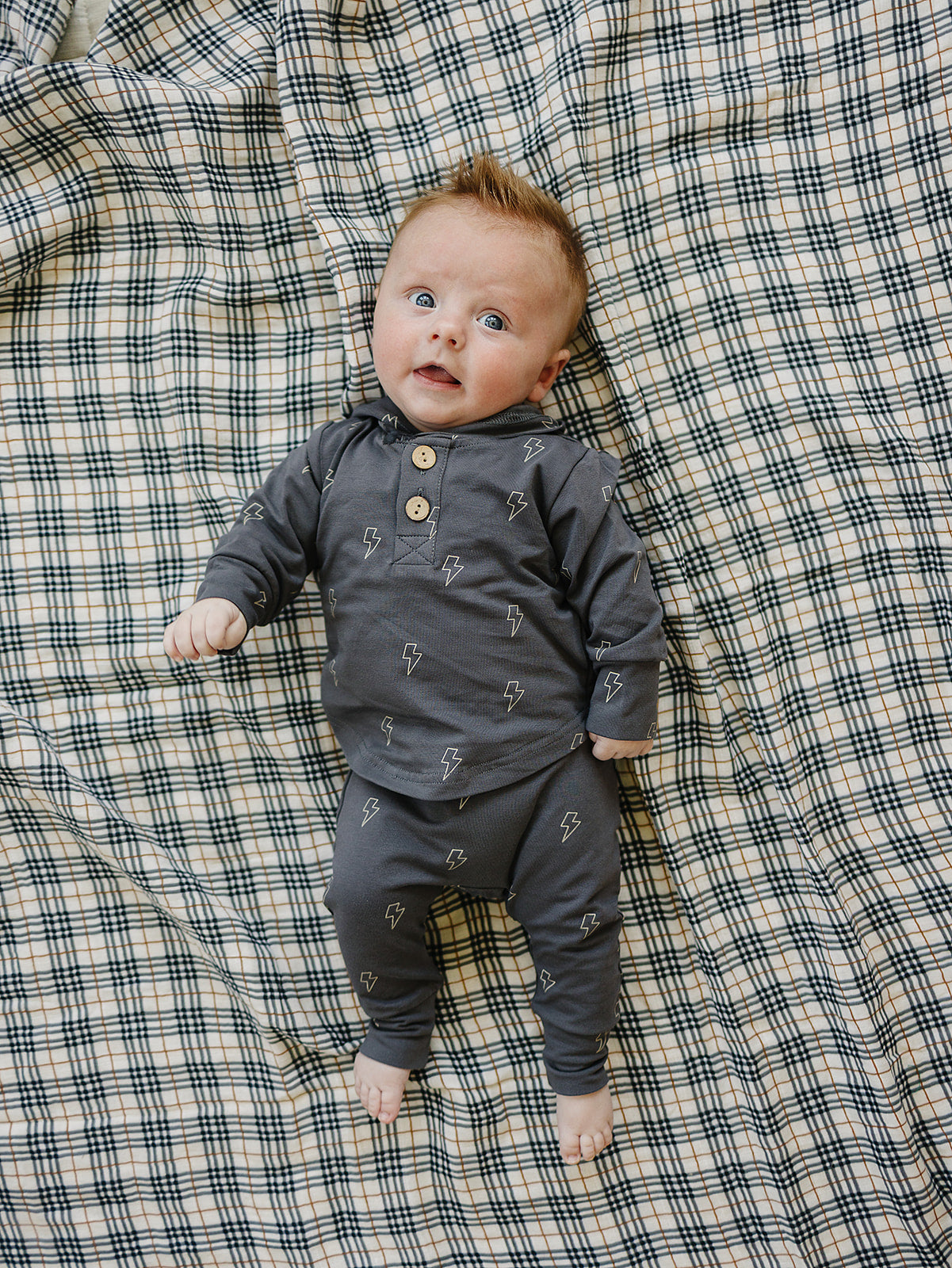 Baby in cozy gray lightning bolt outfit on plaid background, perfect for stylish boys' school attire.