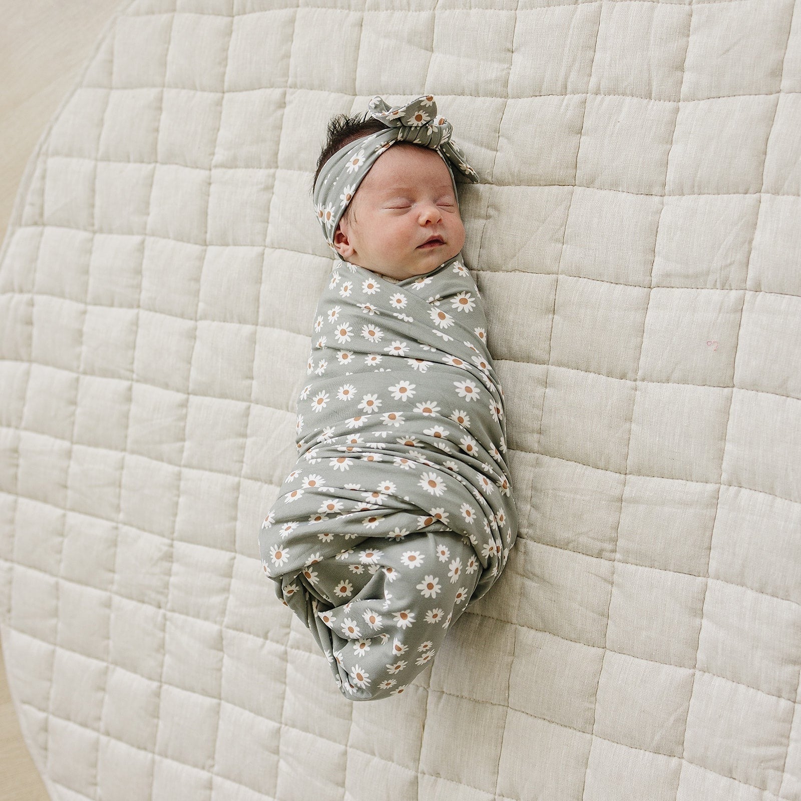 Bamboo Stretch Swaddle Light Green Daisy wrapped around a sleeping baby on a soft quilted blanket.