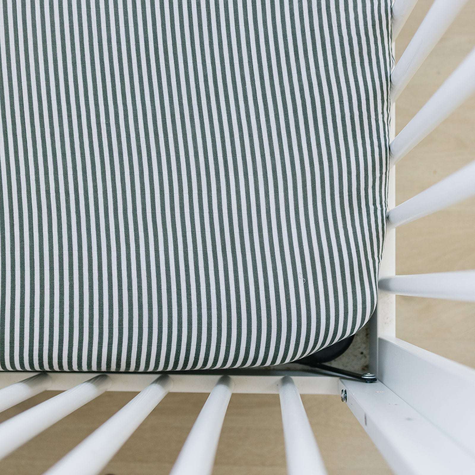 Muslin Crib Sheet with green stripes fitted securely on a standard crib mattress.