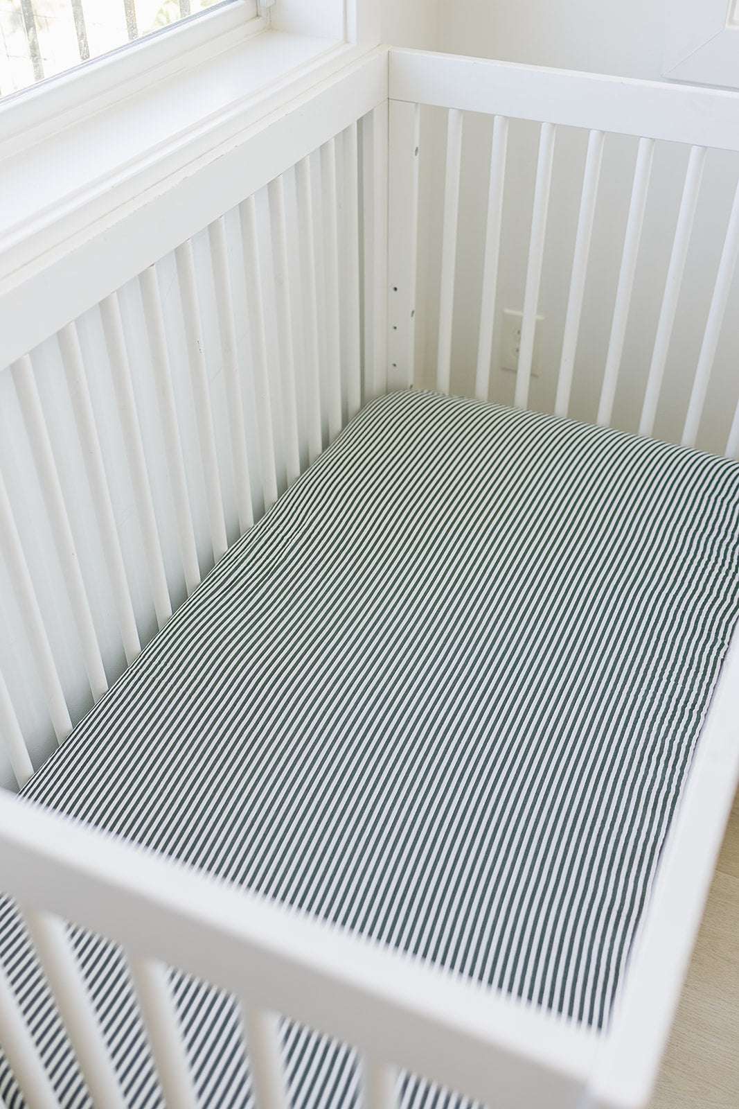 Muslin Crib Sheet in Green Stripes fitted on a standard crib mattress, perfect for a stylish nursery.
