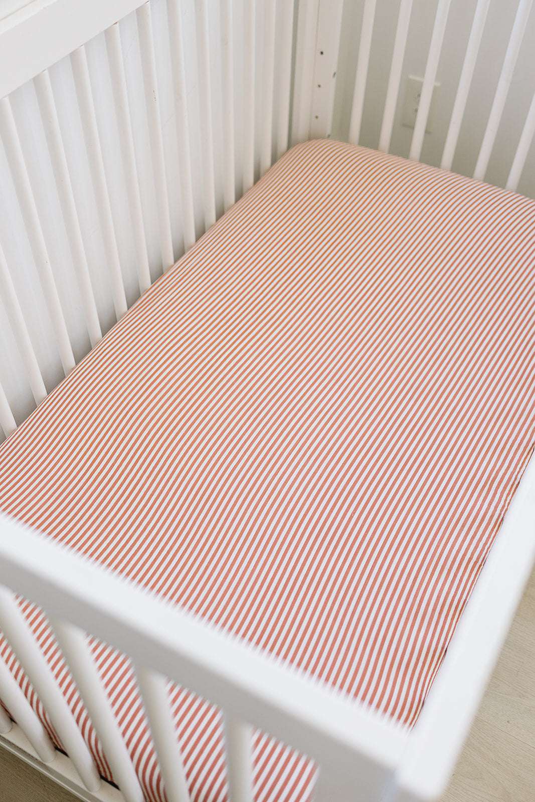 Muslin Crib Sheet Pink Stripes on a white crib mattress, adding style and comfort to a nursery.