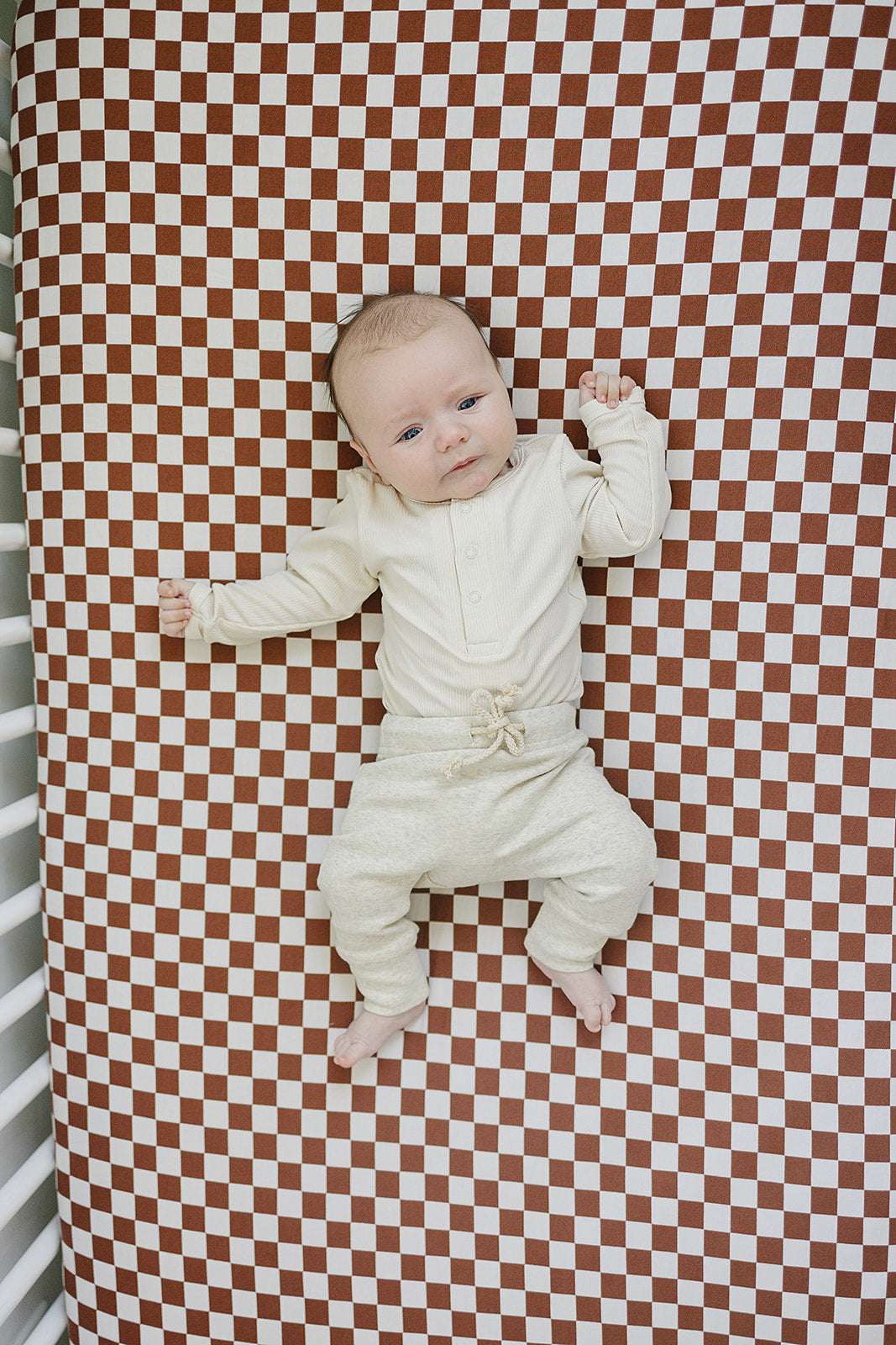 Bamboo Stretch Crib Sheet with rust checkered pattern and a baby laying on it, ideal for a nursery.