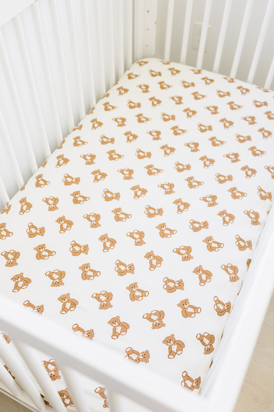 Muslin crib sheet featuring cute teddy bear pattern in a crib, soft and breathable for baby comfort.