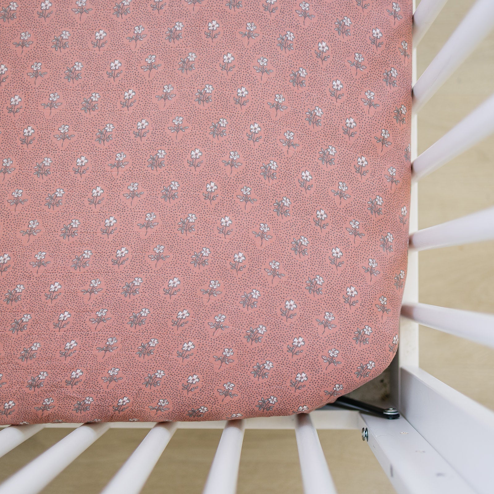 Muslin crib sheet in vintage pink floral design fitted snugly on a crib mattress.