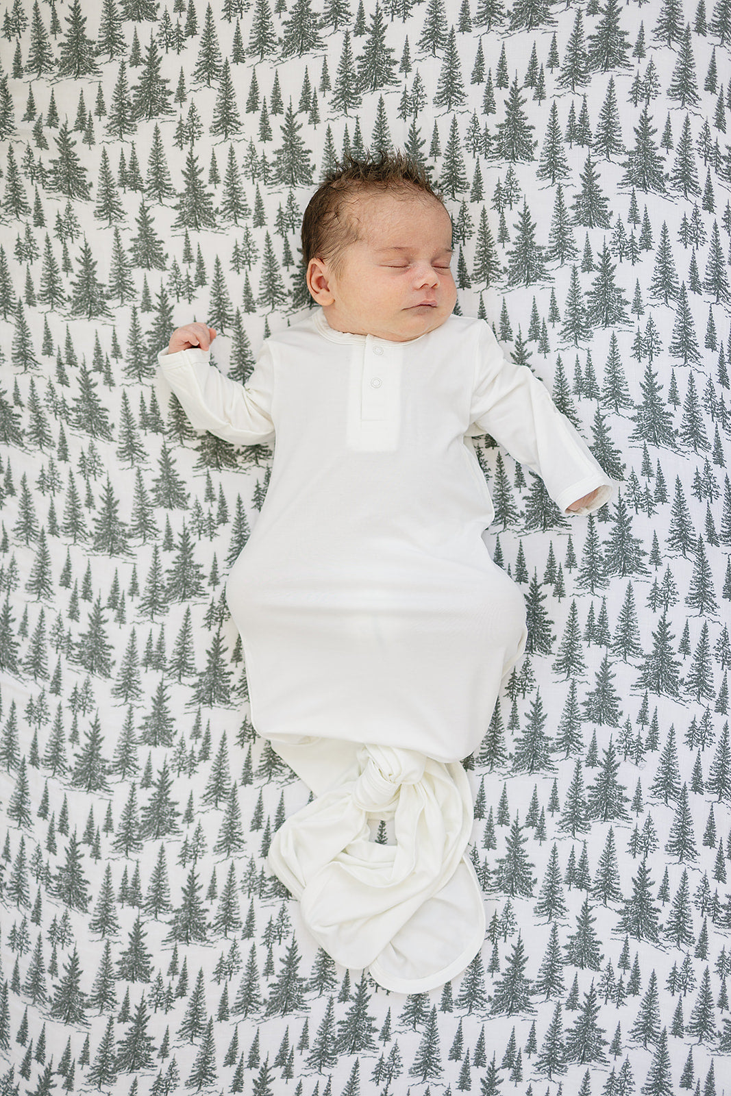 Baby peacefully sleeping on a muslin crib sheet featuring a forest woodlands design, showcasing the softness of muslin crib sheet.