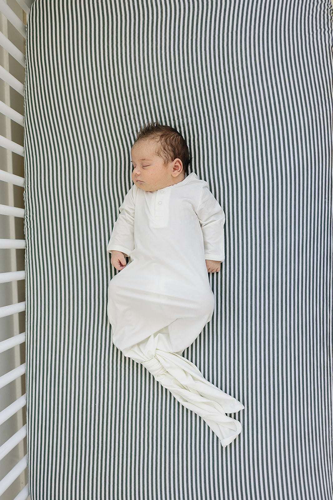 Muslin Crib Sheet featuring soft green stripes with a peacefully sleeping baby on a crib mattress.