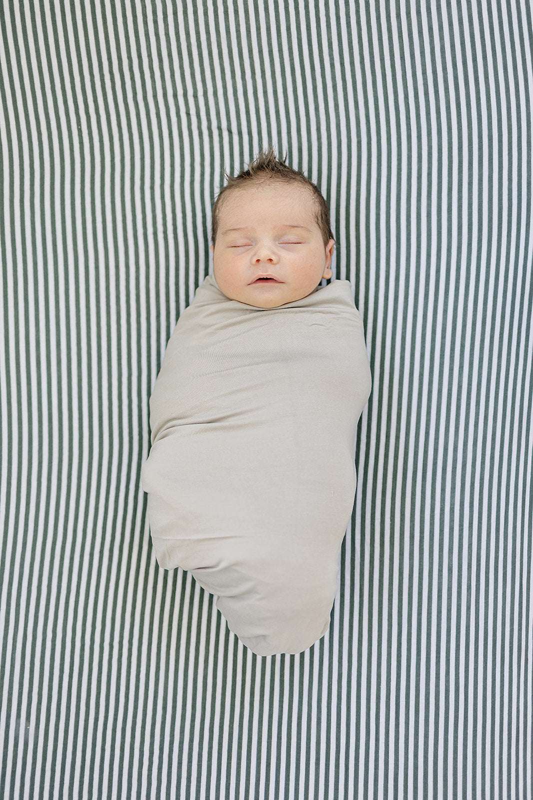 Muslin Crib Sheet - Green Stripes with a swaddled baby sleeping on it, providing a soft and safe environment.