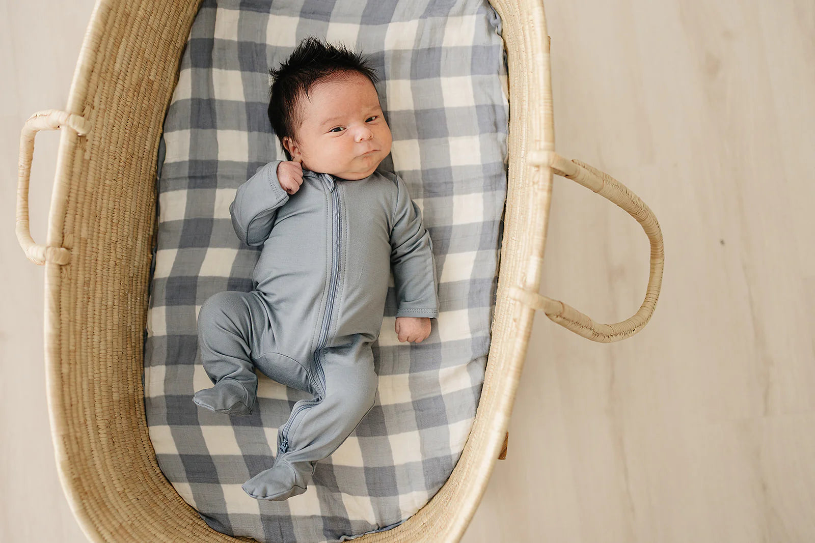 Bamboo baby pajamas dusty blue footed zipper on a baby lying in a wicker basket.