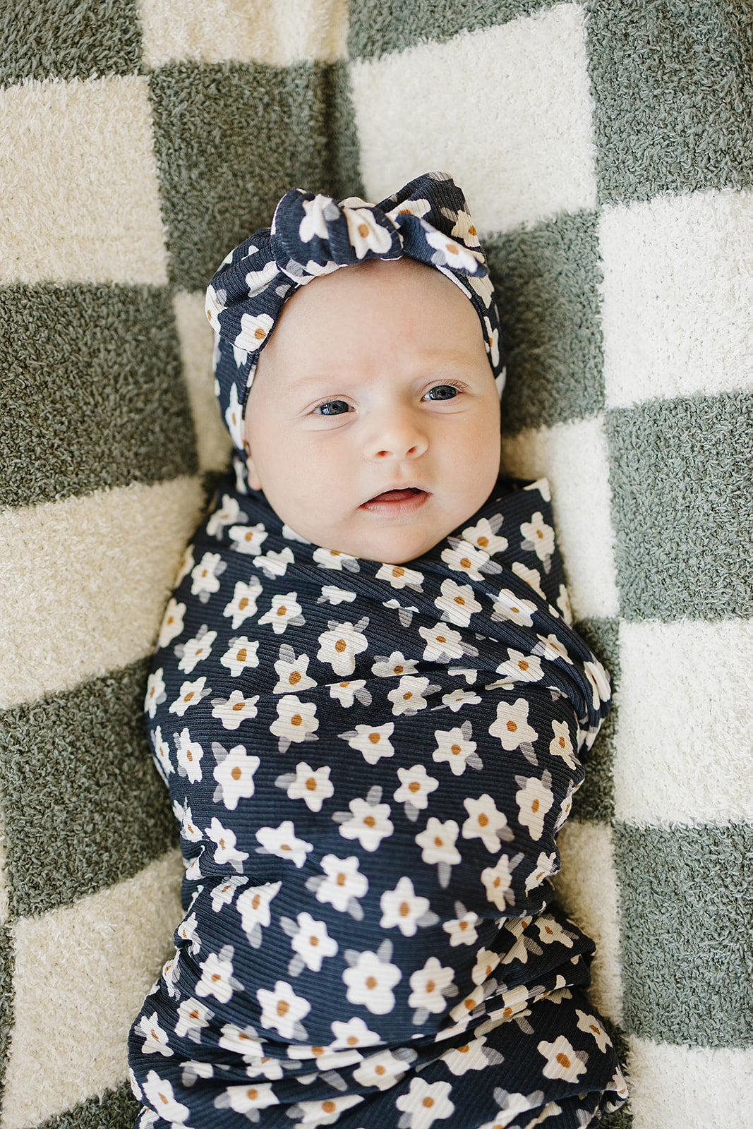 Baby wrapped in Bamboo Stretch Swaddle Navy Daisy Ribbed with matching headband on a cozy blanket.