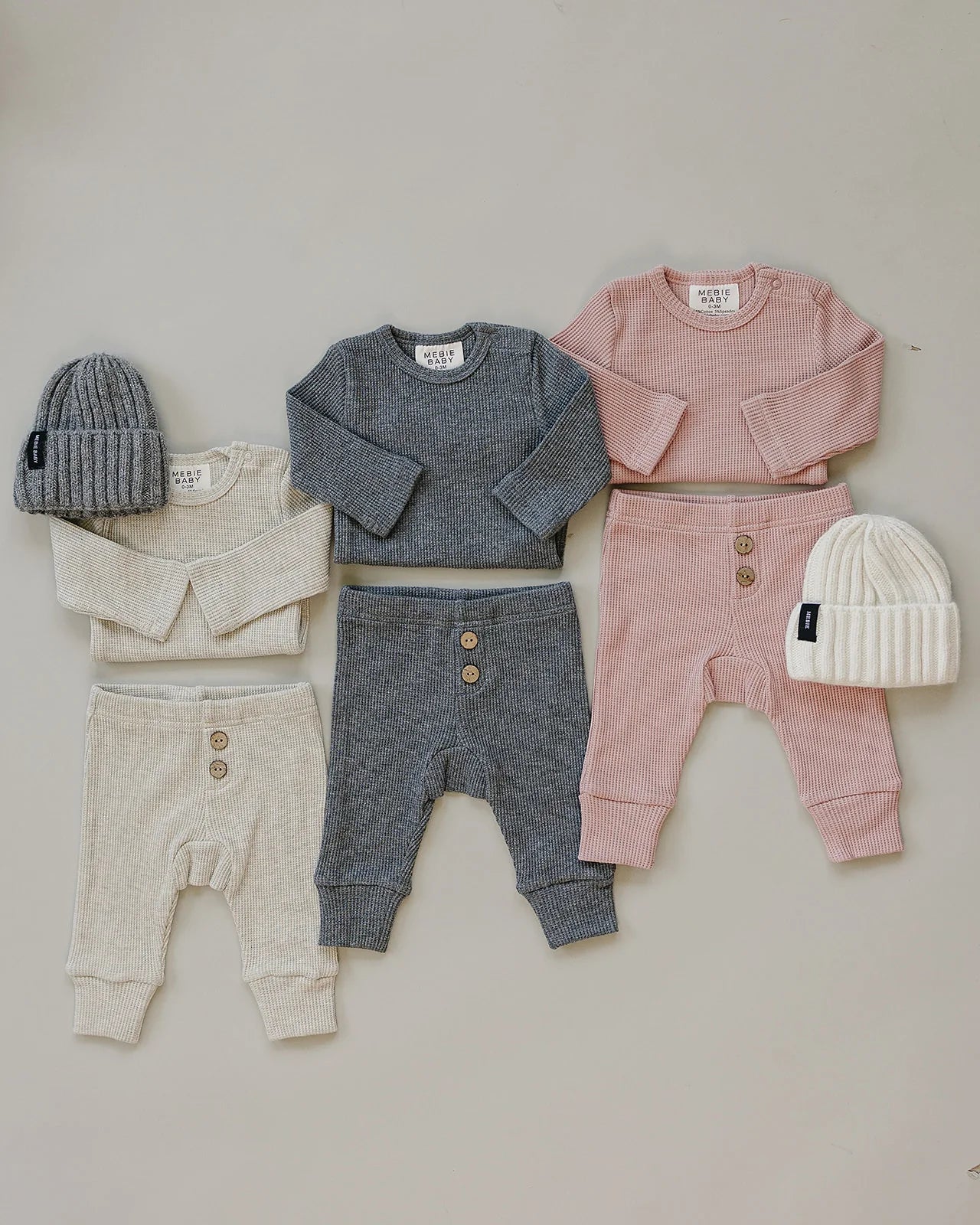 Waffle knit baby bodysuit set in grey, pink, and cream with matching beanies for cozy infant wear.